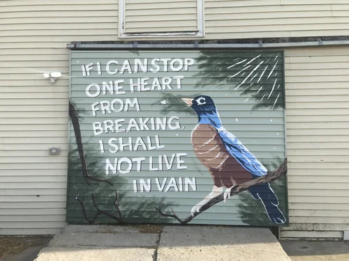 An image of a mural on a large barn door.In it, a robin sits on a branch surrounded by rays of light and simple white butterflies. Text reads: If I can stop one hearts from breaking, I shall not live in vain. A progress gif plays when moused over.